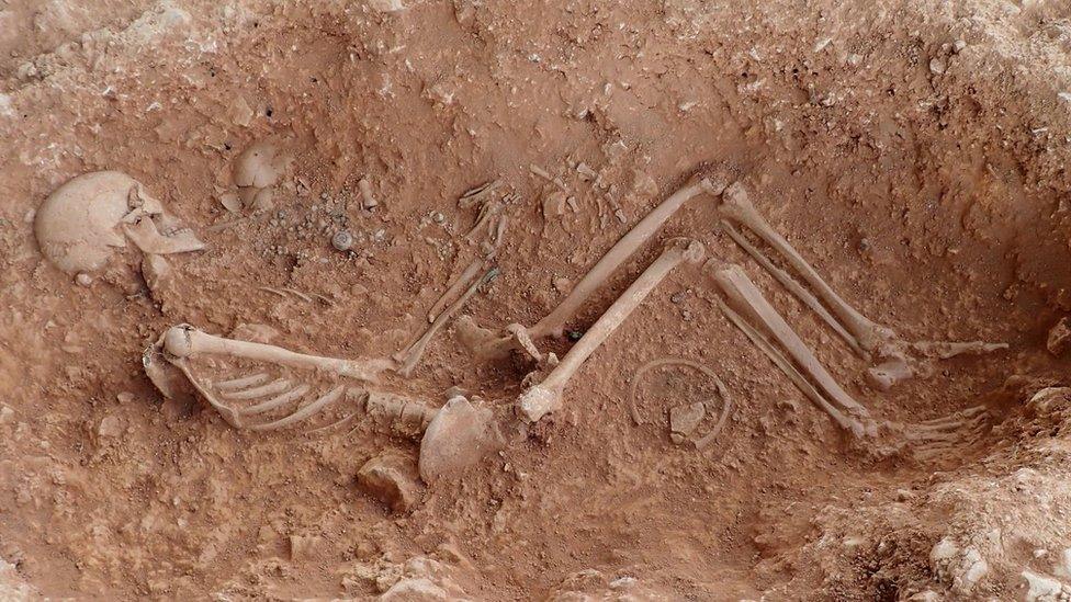 Skeleton of a woman cradling a baby in her left arm buried in the ground