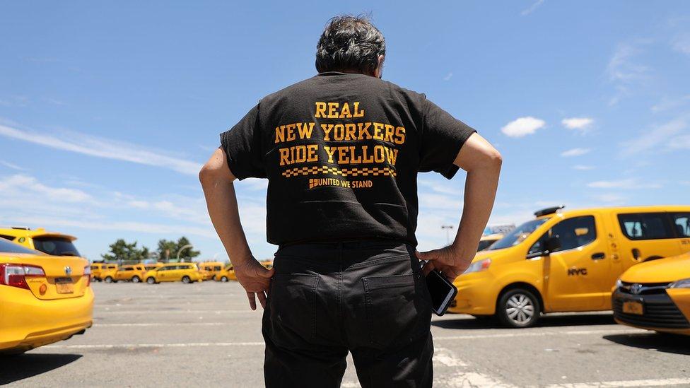 A taxi driver stands in front of Yellow cabs at JFK wearing a shirt that says "real New Yorkers ride yellow"