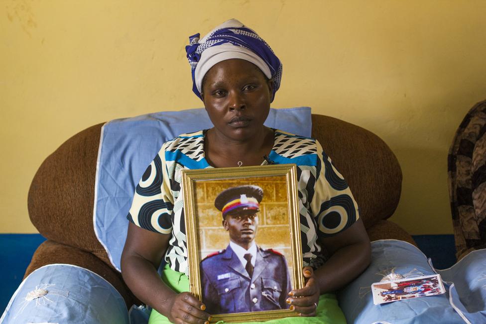 Irene Nduku Kasyoki holds up a portrait of her late husband Geoffrey Kasyoki, a police officer who died trying to save his community's sand