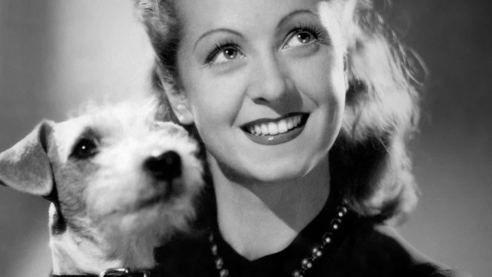 French actress Danielle Darrieux posing with a dog during a photo session in the 1930s