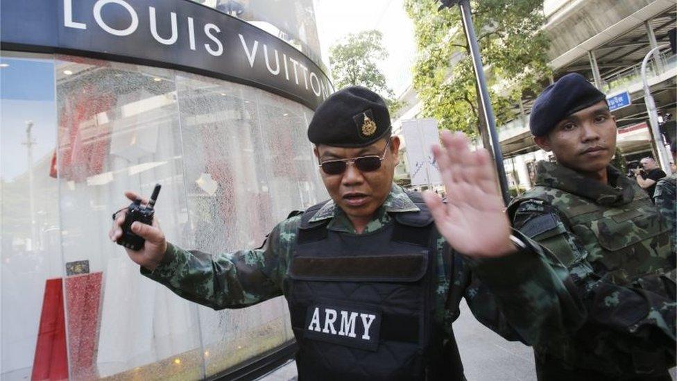 Soldiers move onlookers back from the shattered windows of a Louis Vuitton shop at Gaysorn shopping plaza across from the Erawan Shrine at Rajprasong intersection in Bangkok, Thailand, Tuesday, Aug. 18, 2015, as investigations continue the morning after an explosion.