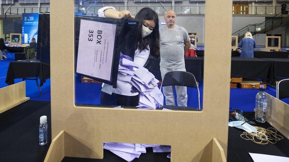 A woman empties lilac ballot papers onto the table, behind a Covid screen