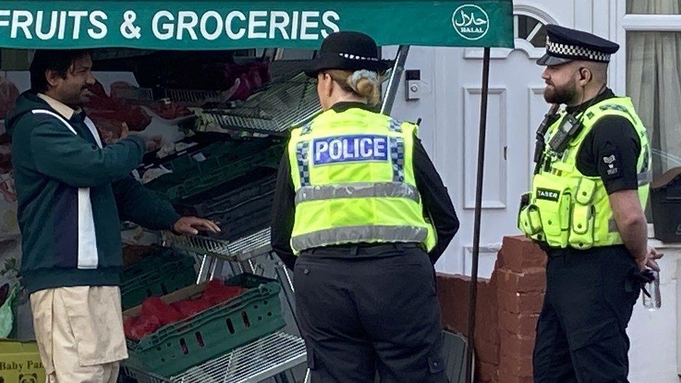 Two police officers in high-vis jackets talk to the owner of a greengrocer