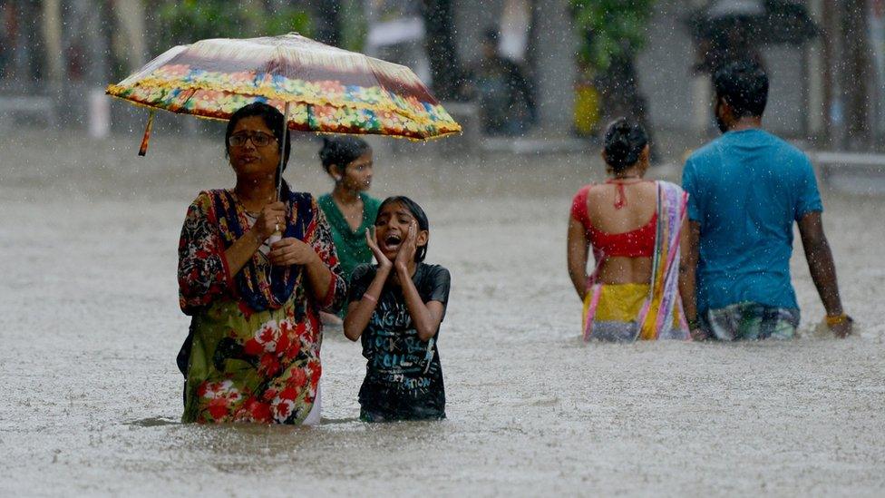 Indians wade through a flooded street during heavy rain showers in Mumbai on August 29, 2017