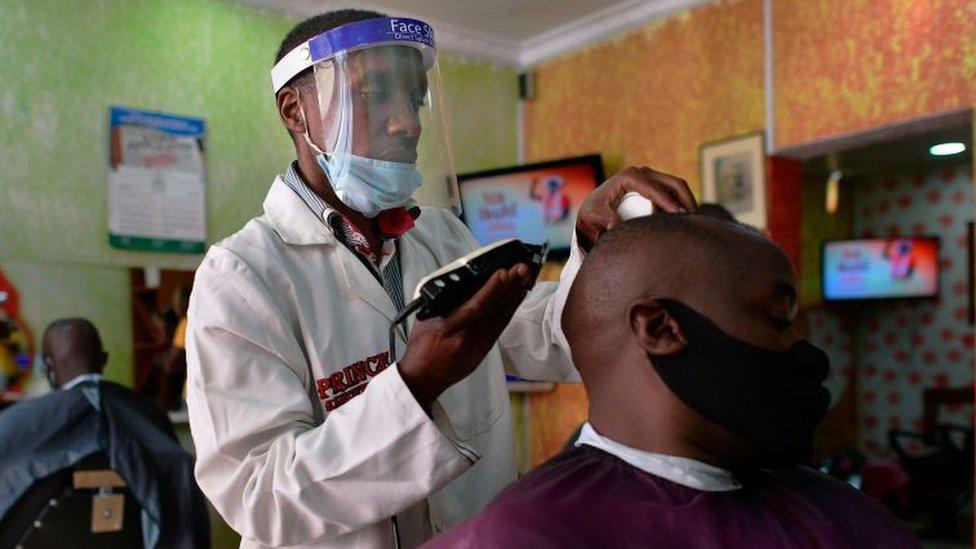 A barber tends to a client while wearing personal protective equipment (PPE) donated by a local youth group comprised of some entrepreneurs who have lost their livelihoods due to the economic slump caused by countrywide restrictions imposed on movement of people and goods, in a bid to curb the spread of the COVID-19 coronavirus, who manufacture personal protective equipment (PPE) in a shed in Waithaka, a suburb of Nairobi on May 14, 2020.