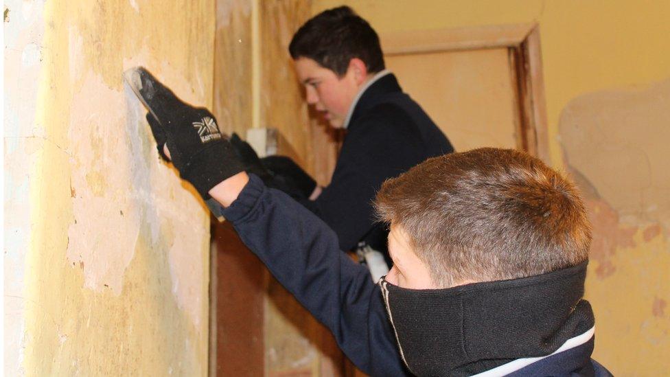 Evan Jones and Luc Jones scraping paint off wall inside building