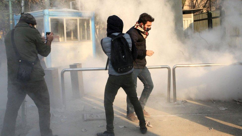 Iranian students run for cover from tear gas at the University of Tehran during a demonstration