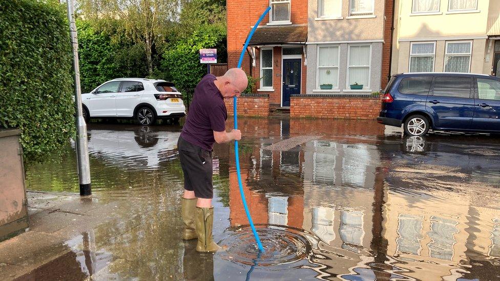 A man putting a pipe down a drain on the corner of Denmark Street, Bedford