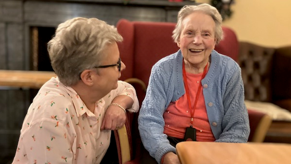 Sally Hebeler sitting with her mother Jocelyn who is laughing and wearing a blue cardigan