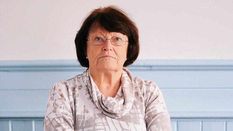 A woman with dark hair in front of a blue panelled wall