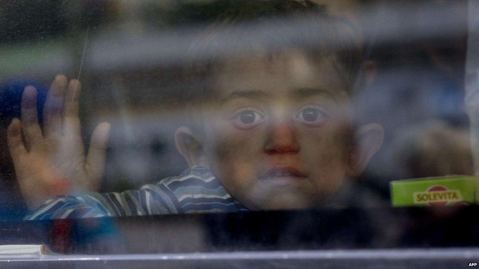 A migrant child waves from on board a train