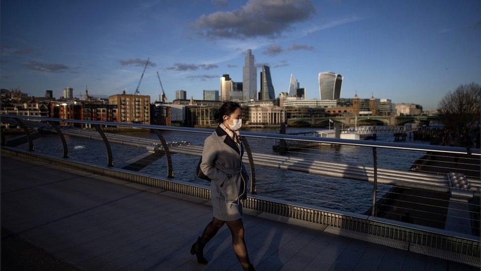 Woman wearing a mask walking on a bridge over the Thames