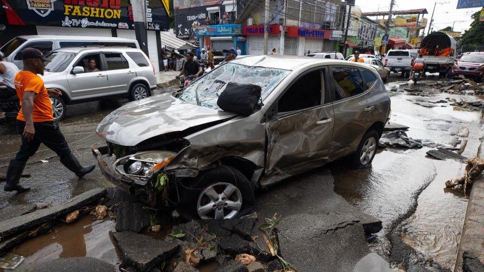 A man walks next to a vehicle that was swept away by the current of rain in Santo Domingo, Dominican Republic, 19 November 2023.