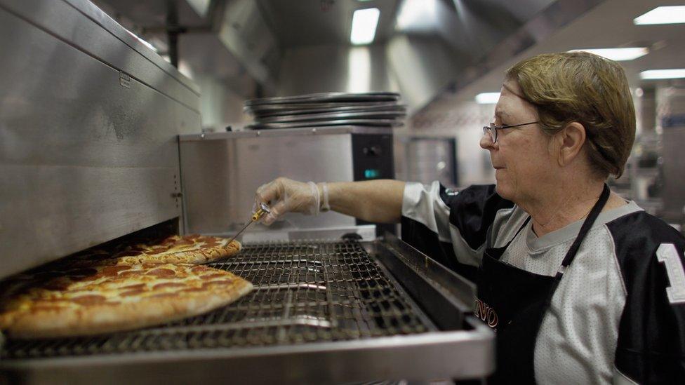 Woman checks the temperature of a pizza during school lunch service