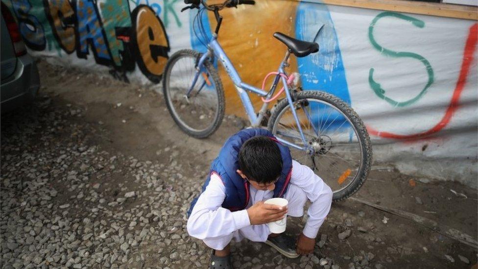 Boy drinks tea outside a cafe in the 'Jungle' migrant camp