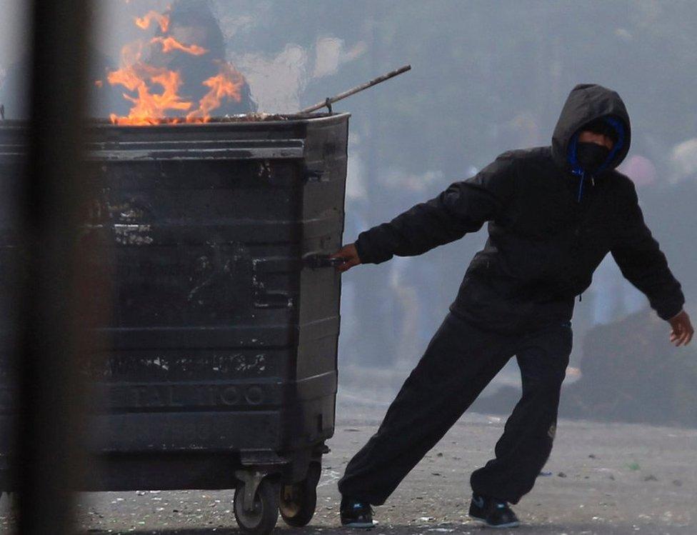 A youth in Hackney pulls a flaming industrial bin set on fire by rioters in east London