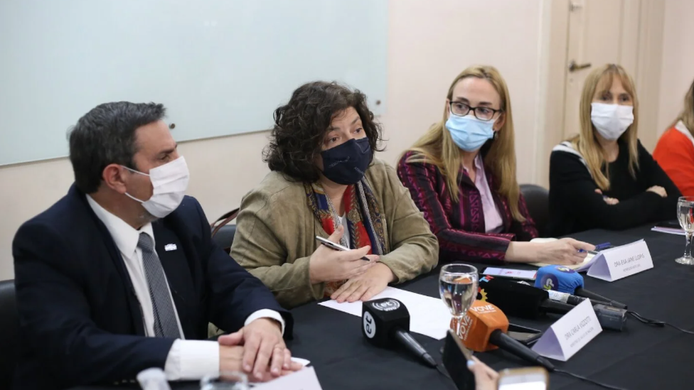 Four health officials, masked, at a press conference answering questions in front of microphones