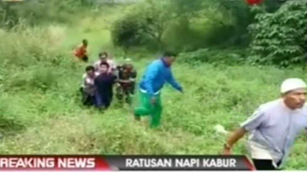 people on green hillside holding a man's hands behind his back and walking him uphill