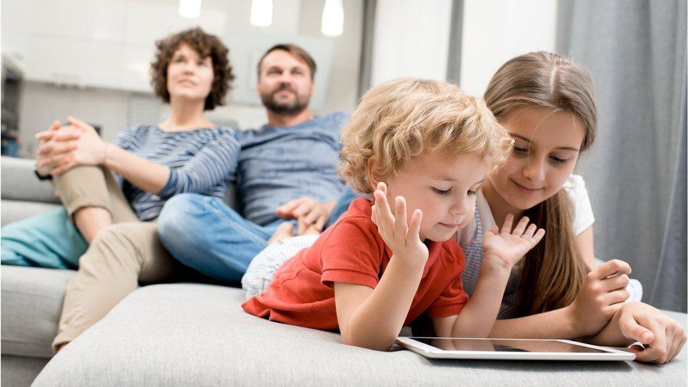 Parents watching TV, children looking at a tablet