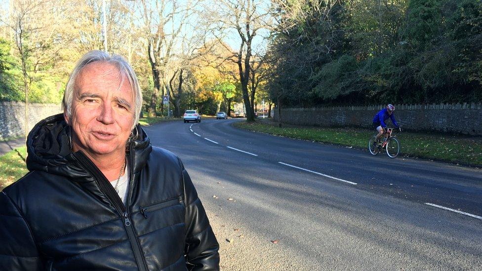 Mark Parkin on Mayals Road in Swansea, with a cyclist about to pass, and mature trees in the background