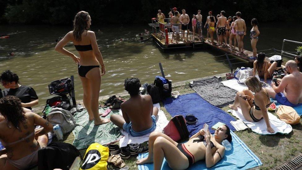 Bathers relax on the perimeter of the mixed-pond on Hampstead Heath in