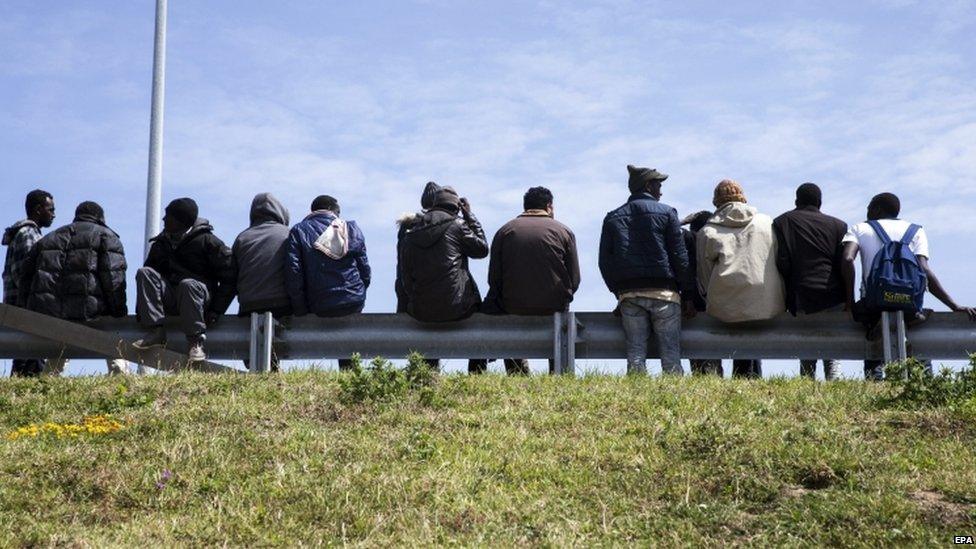 Migrants wait beside a road in Calais