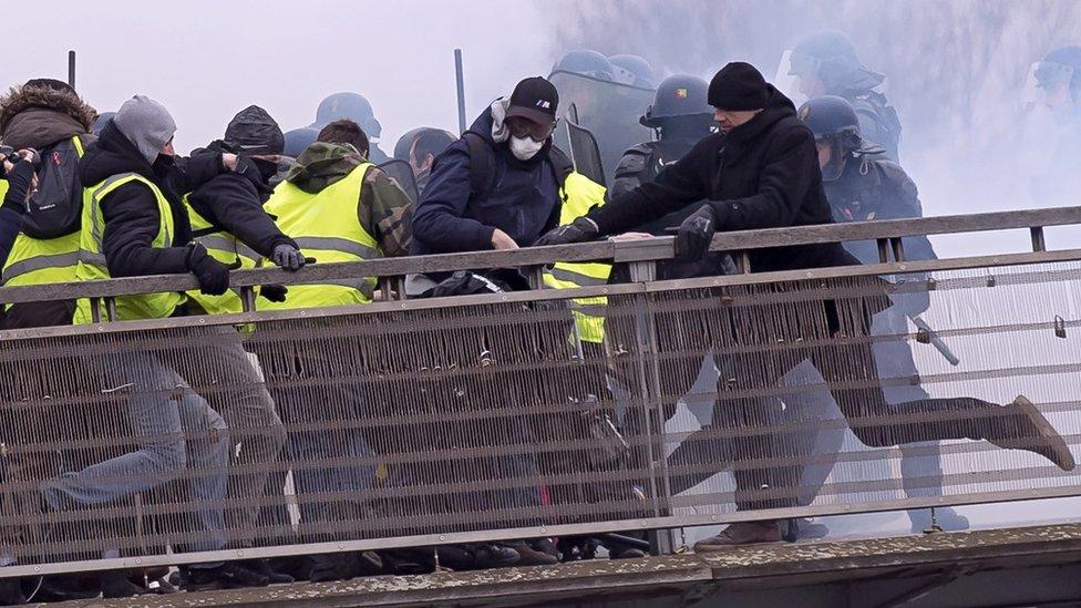 Former French boxing champion Chistophe Dettinger (C, wearing black hat) kicks a French gendarme on the ground during violent clashes on a pedestrian footbridge, during the "Gilets Jaunes" (Yellow Vests) protest in Paris, France, taken 05 January 2019