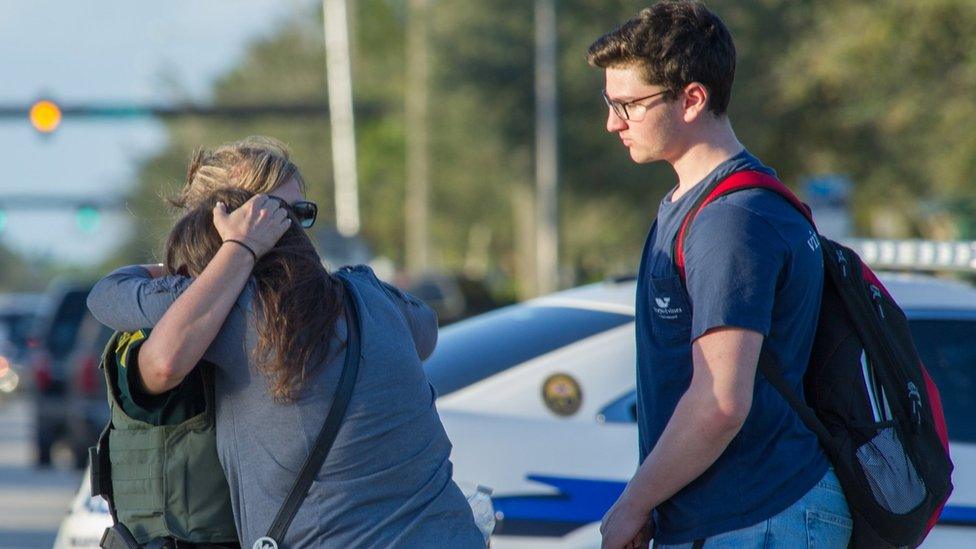 Woman comforted by police officer outside Marjory Stoneman Douglas High School in Parkland, Florida, on 14 February 2018