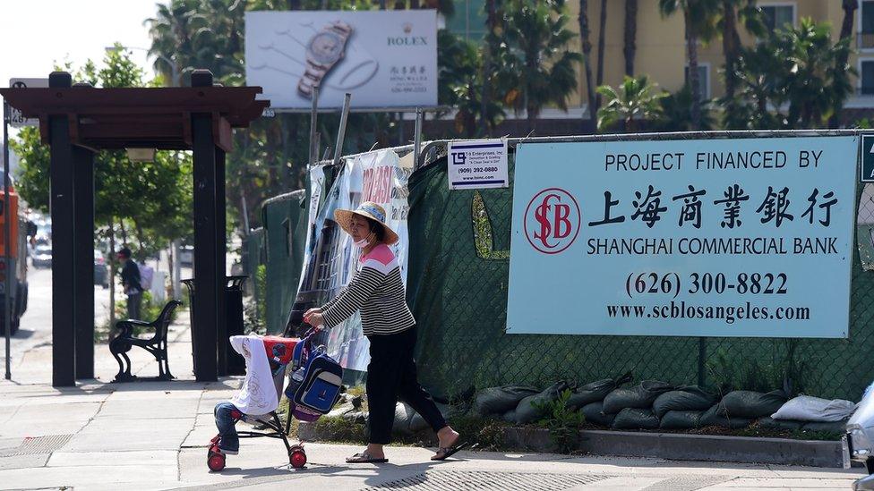 A woman pushes a stroller in San Gabriel, California on May 17, 2016 past a banner at a construction site project financed by the Shanghai Commercial Bank