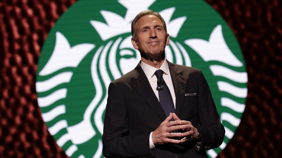 Schultz in front of Starbucks logo onstage in 2017