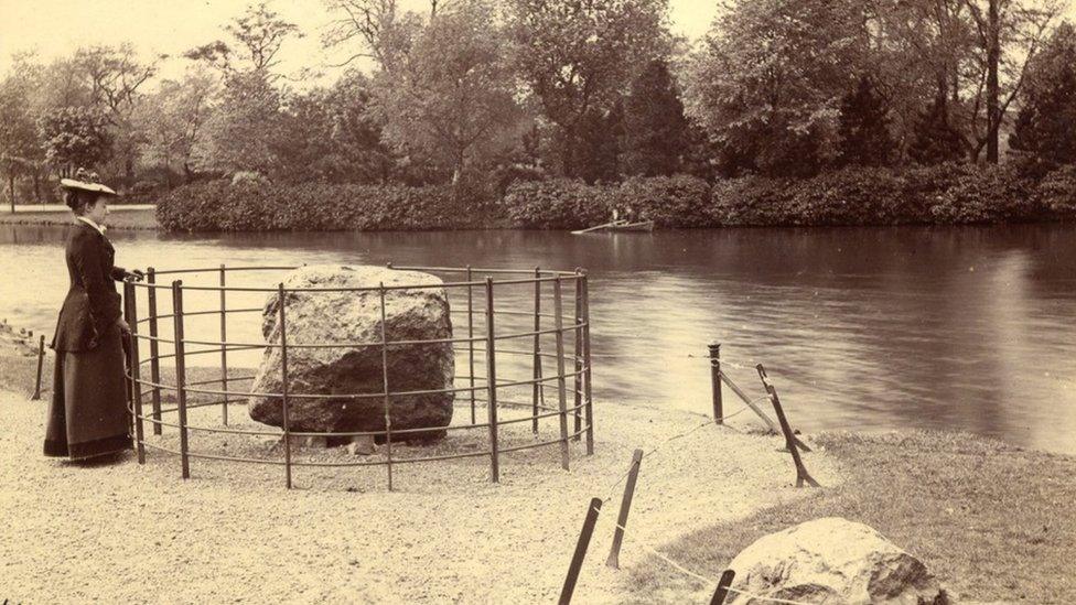 A woman stands next to a boulder in Cannon Hill Park, c.1901