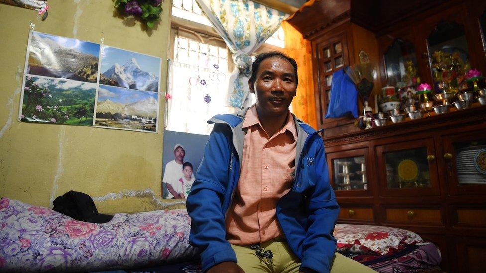 Kami sitting with pictures of Mount Everest in the background.