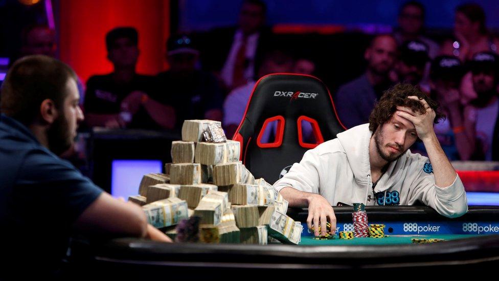 man looking sad next to pile of cash on poker table