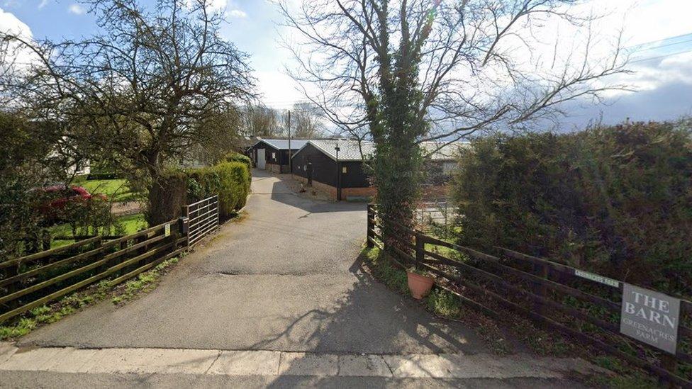 Entrance to farm with low fences either side and trees.