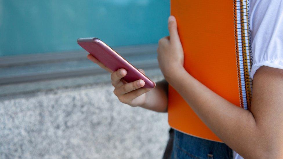 Student girl holding notebooks using her smartphone at the college. Unrecognizable person