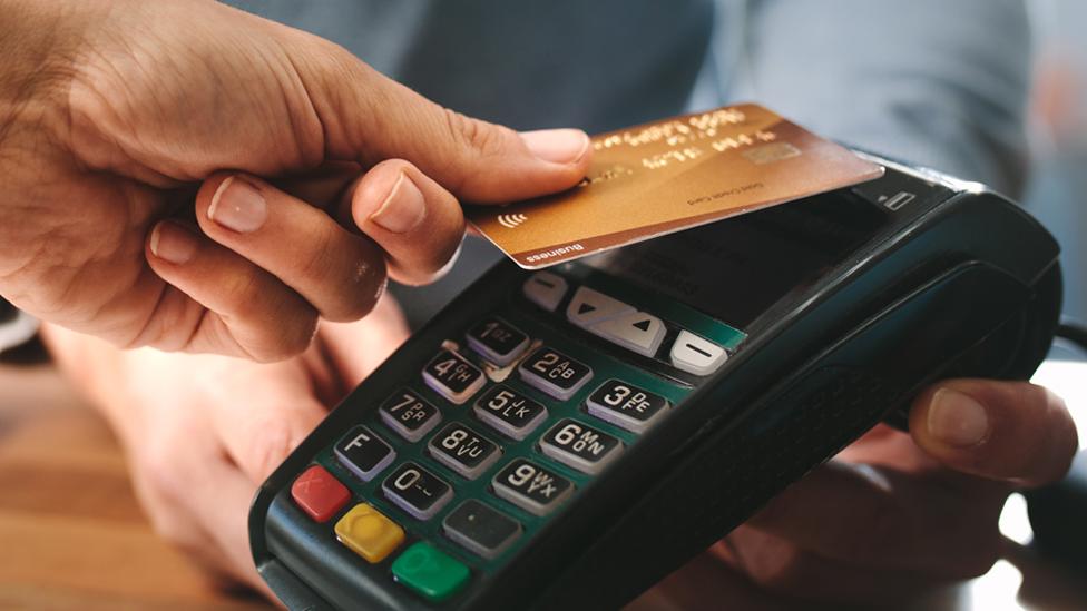 Stock image of a hand holding a credit card, paying using a contactless card reader