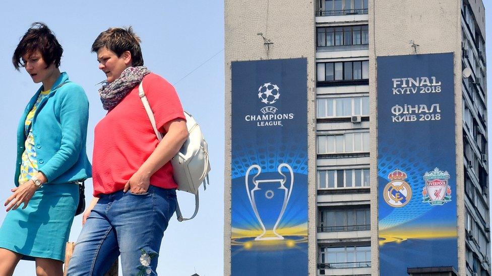 Women walk past a poster of the 2018 UEFA Champions League Final set on a building in Kiev