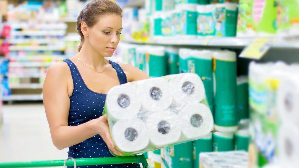 Woman holding toilet paper in supermarket aisle