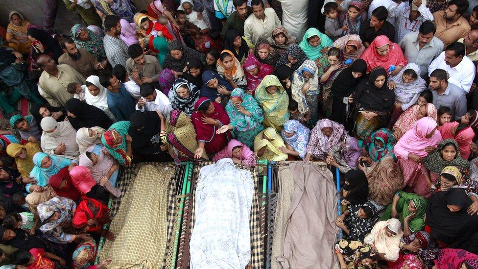 Muslim women and men gathered around three bodies in 2014