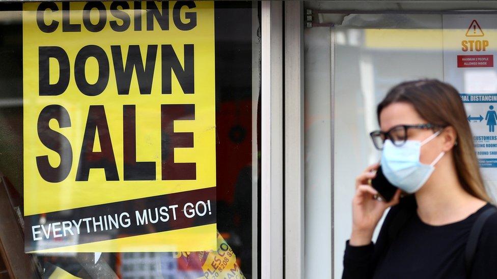 A woman wearing a protective mask speaks on the phone in front of a closed down store