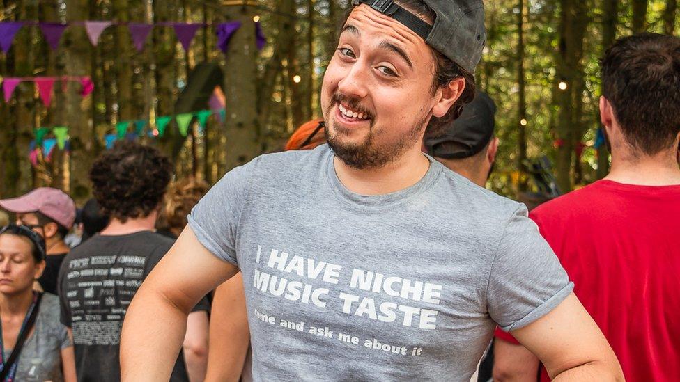 A man wearing a t-shirt that says "I have niche music taste come and ask me about it"