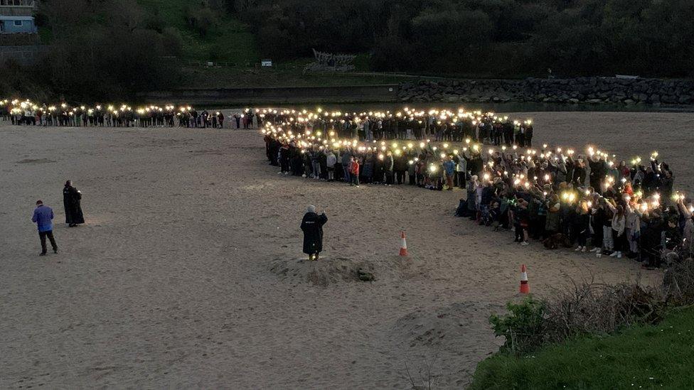 Y gymuned yn chwifio golau gyda'u ffonau symudol ar y traeth