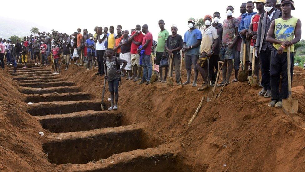 Men wait beside empty graves for the coffins of mudslide victims at Waterloo cemetery near Freetown