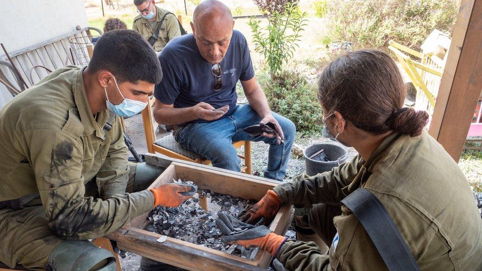 An Israeli archaeologist and two soldiers inspect a sieve containing debris from house in southern Israel that was set on fire during Hamas's attack on 7 October