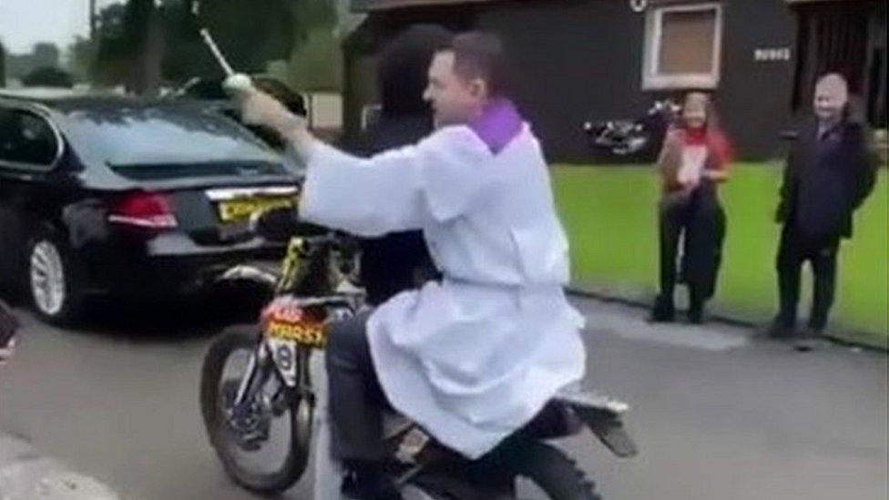 priest sprinking holy water behind bike rider