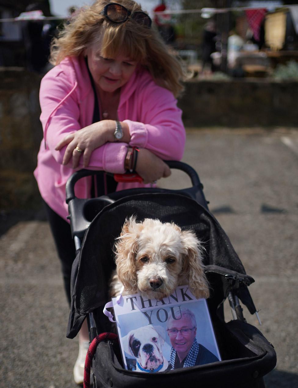 A person waits outside the Walnut Tree Pub with a dog in a pram and a picture of Paul O'Grady with the words "Thank you"