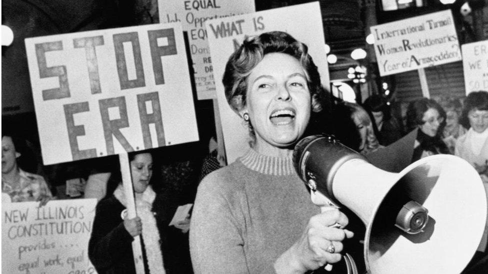 Phyllis Schlafly with protesters behind her holding signs saying 'Stop ERA'