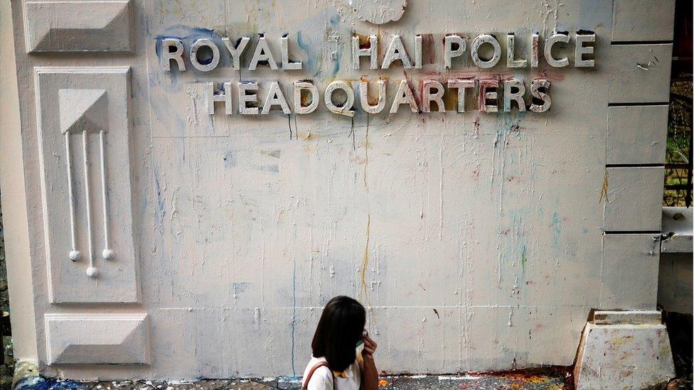 A woman reacts while walking past the damaged signage of the police headquarters