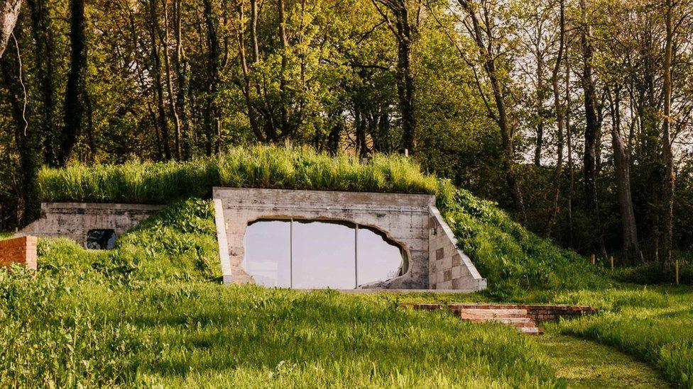 A refurbished concrete bunker covered in grass with a glazed blast opening