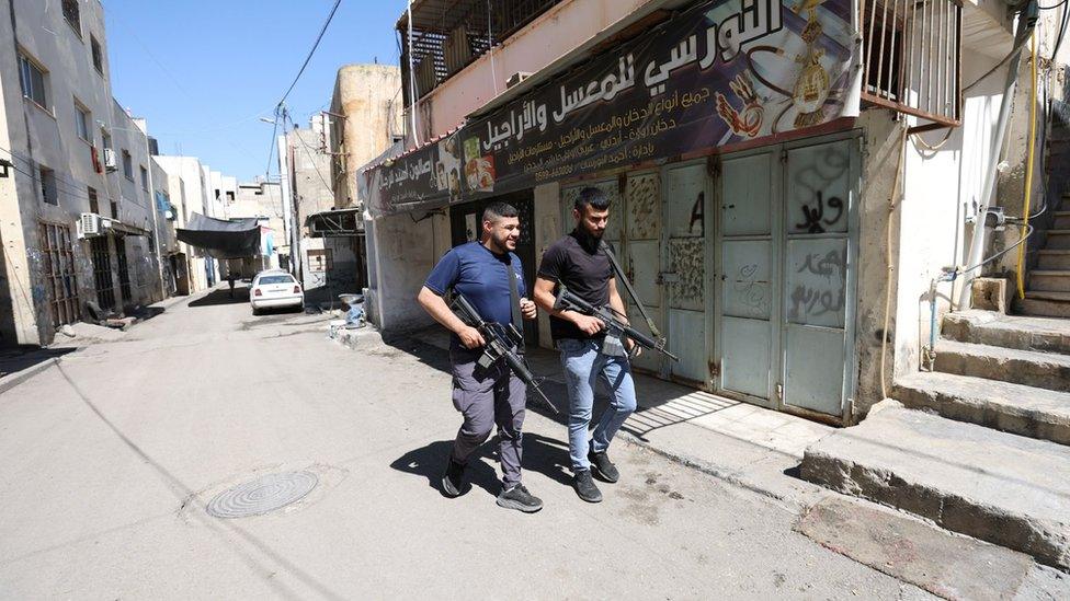 Palestinian militants walk along a street inside Jenin refugee camp, in the occupied West Bank, ahead of a visit by President Mahmoud Abbas (12 July 2023)